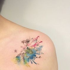 a woman's shoulder with a watercolor tinkerbell tattoo design on it