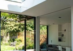 a living room filled with furniture next to a large glass window covered in plants and trees