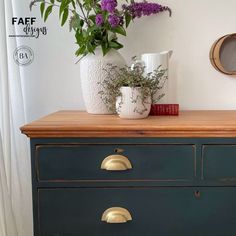 a green dresser with flowers on top and a white vase sitting on top of it