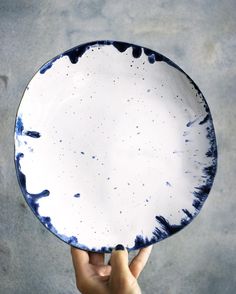 a person holding up a white and blue plate with black spots on the rims