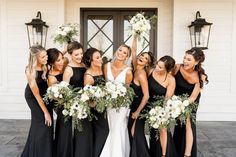 a group of women standing next to each other in front of a white building holding bouquets