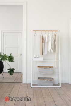 an empty room with clothes hanging on racks and a plant in the corner next to it