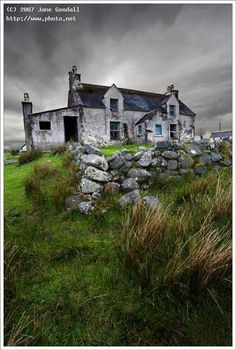 an old house sitting on top of a grass covered hill next to a stone wall