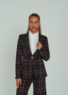 a woman in a black and brown plaid suit posing for the camera with her hand on her hip