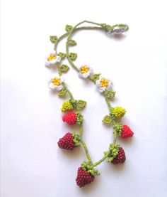 a crocheted necklace with flowers and berries hanging from it's side on a white surface