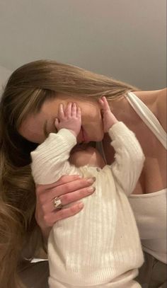 a woman holding a baby in her arms and kissing it's face with both hands