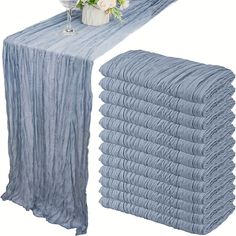 a stack of blue cloths next to a vase with flowers on it and a table runner