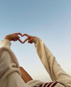 two hands in the shape of a heart against a blue sky with white clouds above