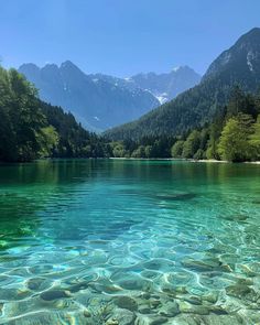 clear water with mountains in the background and trees on both sides, surrounded by rocks