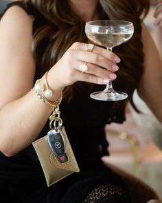 a woman holding a wine glass with a keychain attached to it and wearing pearls