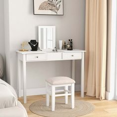 a white desk with a mirror and stool in front of a window next to a bed