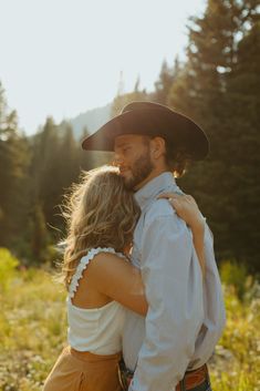 a man and woman in cowboy hats embracing each other while standing in tall grass with trees in the background