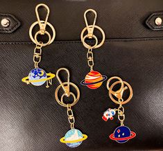 four keychains with different designs on them hanging from a black purse, one is gold and the other two are planets