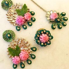 three brooches with pink flowers and green leaves on a white surface, next to a chain