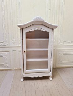 a small white cabinet sitting on top of a hard wood floor next to a wall