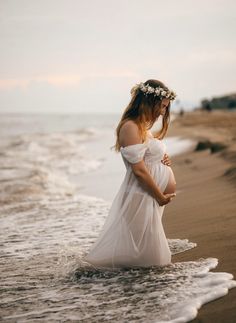 a pregnant woman standing in the ocean with her hands on her belly and wearing a flower crown