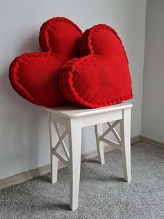 two red heart shaped cushions sitting on top of a white stool