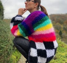 a woman wearing a colorful sweater and black leather pants is posing for the camera with her hand on her chin