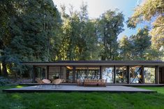 a modern house in the woods surrounded by green grass and trees, with large windows on each side