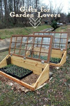 two wooden greenhouses filled with plants in the middle of some grass and leaves on the ground