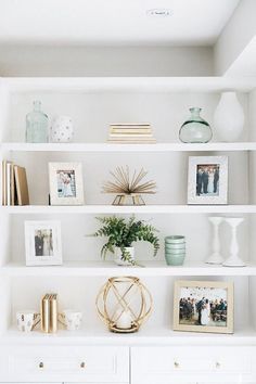 a white book shelf with pictures, vases and other items sitting on top of it