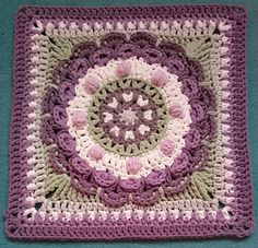 a crocheted square with pink and white flowers in the center on a blue surface