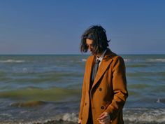 a man in an orange coat standing on the beach