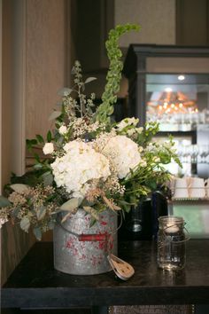 a metal bucket with flowers and greenery on a table