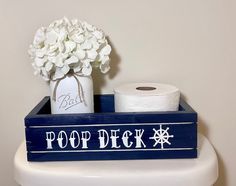 a blue and white wooden sign that says poop deck on it next to a roll of toilet paper