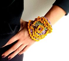 a close up of a person's hand wearing a crocheted bracelet with flowers on it