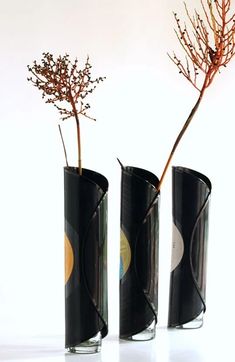 two black vases with flowers in them on a white surface, one is empty and the other has no leaves