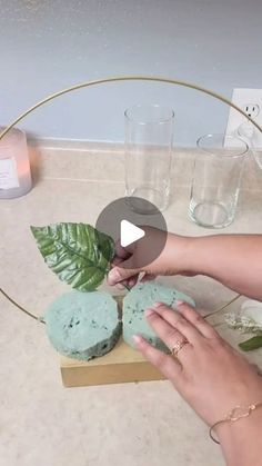 a woman is decorating some cookies with blue icing and green leaves on the table