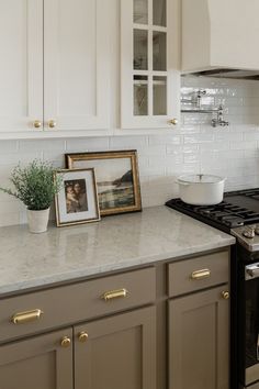 a kitchen with white cabinets and marble counter tops, gold trim around the stovetop