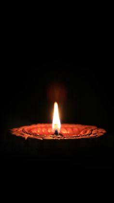 a candle is lit in the dark on a wooden plate with some water droplets around it