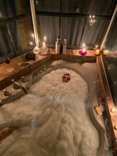 a bathtub filled with lots of white foam next to candles and bottles on the floor