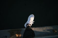 someone's feet in white sneakers standing on the edge of a dock