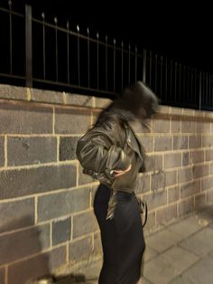 a woman is walking down the street in front of a brick wall with an umbrella