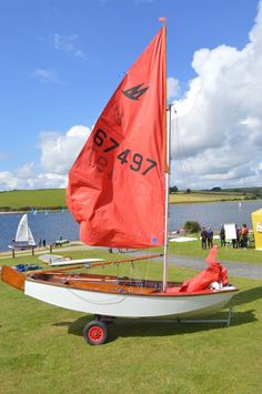 a small sailboat is parked on the grass near some water and people are in the background