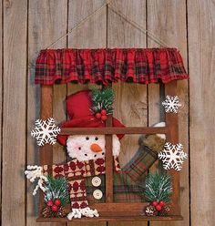 a snowman in a window hanging on the side of a wooden fence with christmas decorations