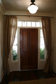 a wooden door sitting inside of a room next to two windows with curtains on them