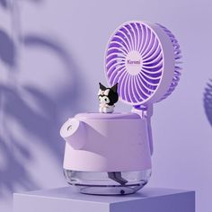 a small cat sitting on top of a table next to a purple fan