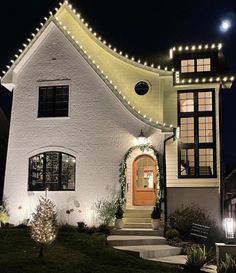 a white house with christmas lights on the roof and stairs leading up to it's front door