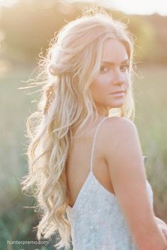 a woman with long blonde hair standing in a field looking at the camera while wearing a white dress