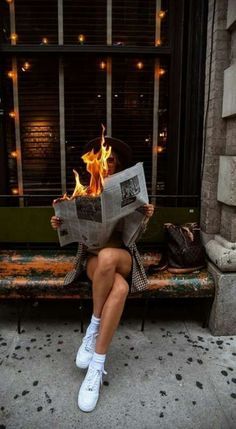 a woman sitting on a bench reading a newspaper while holding a fireball in her hand