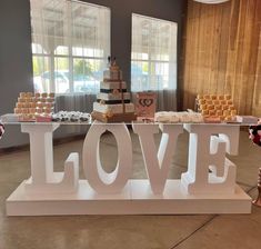 a table topped with lots of cakes and cupcakes next to a sign that says love