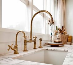 a kitchen with marble counter tops and gold faucets on the sink, next to a window