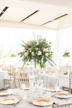 a table set up with plates, silverware and flowers in a tall glass vase