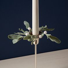 a white candle with green leaves and berries on it