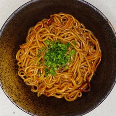 a black bowl filled with noodles and green onions