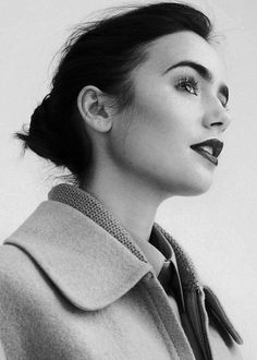 a black and white photo of a woman wearing a coat with her hair in a bun